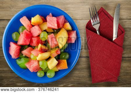 Fruit Salad On A Brown Wooden Background. Vegetarian Salad Of Fruit On A Blue Plate With Fork Ank Kn