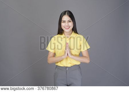 Beautiful Confident Woman Is Greeting (thai Wai) To Show Respect Over Grey Background Studio