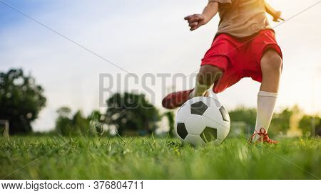 Boy Kicking A Ball While Playing Street Soccer Football On The Green Grass Field For Exercise. Outdo