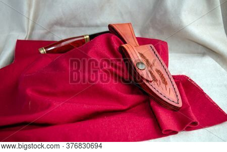 A Uniquely Decorated Leather Sheath Is Displayed On A Red Fabric While The Knife Sits In The Backgro