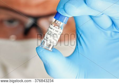 Hand In Blue Medical Gloves Holding Small Vial With Label That Says Cov2 Vaccine (sticker Is Own Des