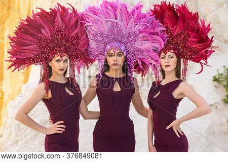 Girls In Crowns Of Feathers Pose On A Rock. Brazilian Carnival