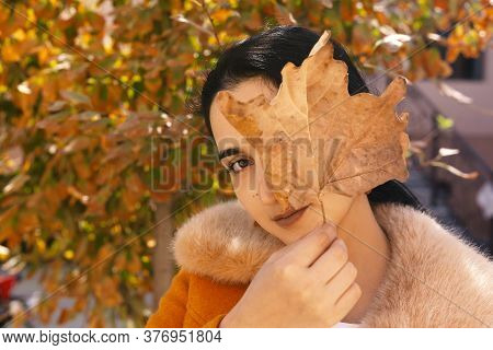 Autumn Portrait Of Cute Arabian Woman Covering One Eye With Big Fall Leaf. Autumn Garden And Beautif