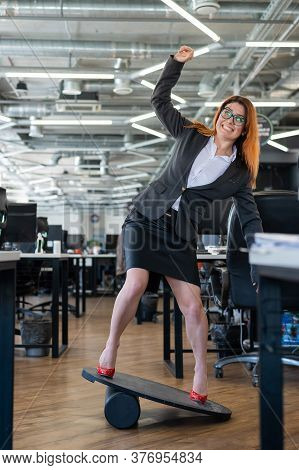 A Woman In A Suit Is Engaged On A Rocker-skateboard During A Break At Work. A Female Office Employee