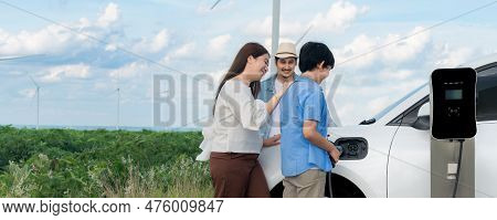 Concept Of Progressive Happy Family Enjoying Their Time At Wind Farm With Electric Vehicle. Electric