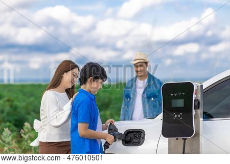 Concept Of Progressive Happy Family Enjoying Their Time At Wind Farm With Electric Vehicle. Electric