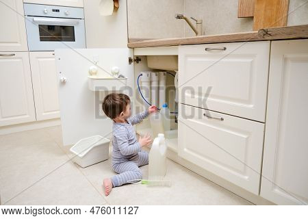 A Child Is Playing With Chemical Cleaning Products Under The Sink In The Kitchen. Baby Holds Bottles