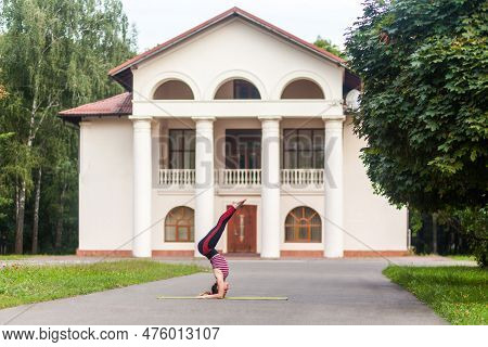 Full Length Side View Of Young Strong Sporty Woman Doing Yoga Asana Supported Headstand On The Stree