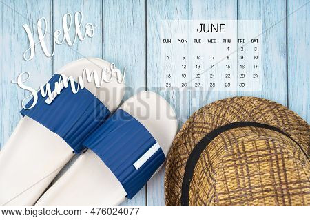 Hello Summer June 2023 Calendar And Blue Rubber Slipper With Brown Straw Hat On Blue Background.