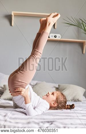 Cute Little Girl Doing Workout In Bedroom At Home On Bad Having Fun Raised Her Legs Keeps Hands In H
