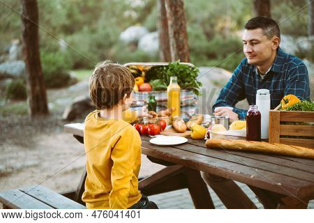 Father Dad And School Kid Boy Child Having A Picnic In The Forest Camping Site With Vegetables, Juic