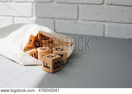 Wooden Cubes With Black Letters Poured Out Of A Cloth Bag On A Gray Table. Front View