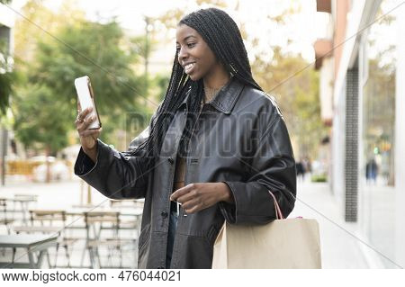 Happy Young Woman Taking A Videocall On Phone In The Street Holding A Shopping Bag. Happy Female Usi