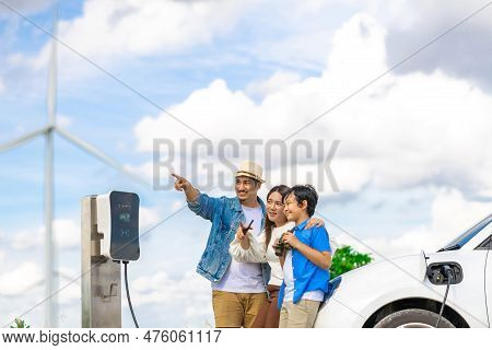 Concept Of Progressive Happy Family Enjoying Their Time At Wind Farm With Electric Vehicle. Electric