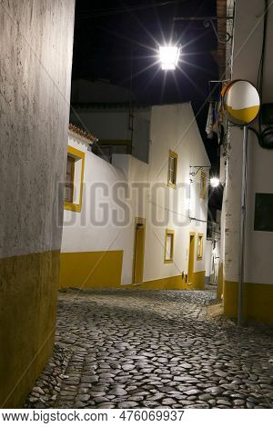 Typical Portuguese Facades And Cobblestone Streets At Night In Evora Town, Portugal