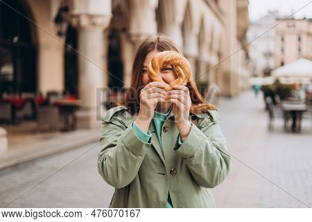 Attractive Young Female Tourist Is Holding Prezel, Traditional Polish Snack On The Market Square In 