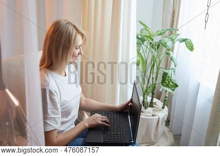 Young Blonde Woman Using Laptop Computer At Home. Girl Is Resting, Chating And Looking In Camera Nea