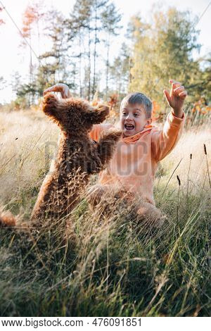 A Boy With A Small Brown Dog Plays In A Meadow With Tall Grass. Leisure With A Pet In Nature. Front 