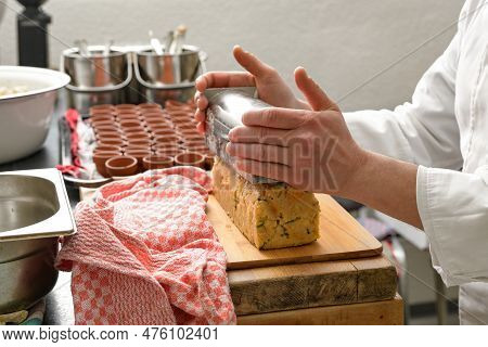 Hands Of A Cook Toppling A Savory Bread Pudding From A Stainless Steel Mold Onto A Wooden Board In A