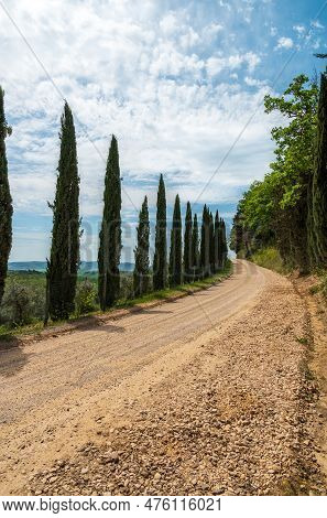 A Dirt Rocky Road Meanders Between Tuscan Cypresses And Goes Beyond The Horizon Under A Beautiful Bl
