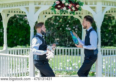 Gay With Partner Open Champagne. Gay Couple Holding Bouquet Of Flower Together During Wedding Ceremo