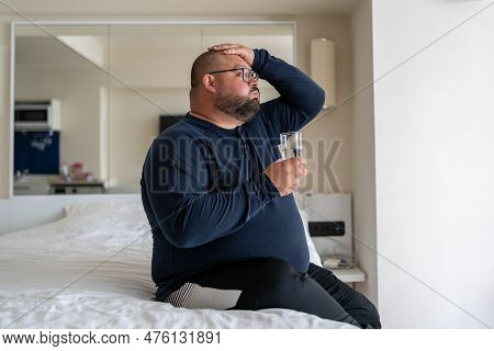 Sad Overweight Bearded Man Suffering From Strong Headache Or Migraine Sit In Bed At Home. Upset Guy 