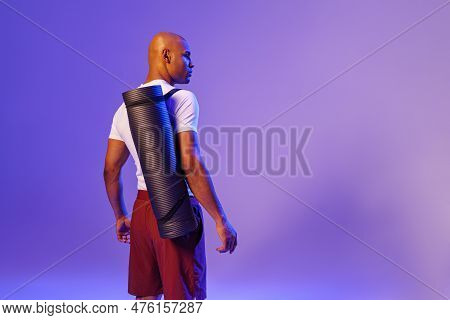Back View Of Fitness Man Holding Rolled Up Exercise Mat On Studio Background With Color Filter
