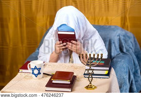 A Jewish Woman In A Kisui Rosh Headdress And A Prayer Veil Kisses The Siddur. Horizontal Photo.