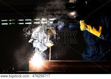 Metal Welder Working With Arc Welding Machine To Weld Steel At Factory While Wearing Safety Equipmen