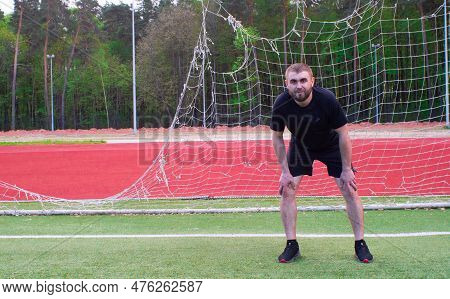 A Male Goalkeeper Stands On The Field In A Straight Football Goal. A Man Plays Football Against The 