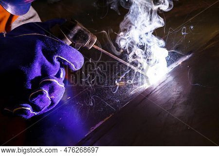 A Welder In A Welding Mask And Gloves Welds With Electric Arc Welding Using Electrodes On Metal.