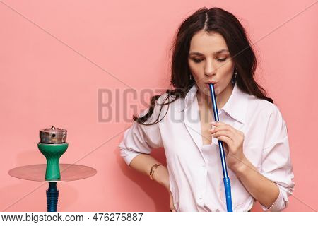 Young Woman Smokes A Hookah, Sheesha On A Pink Background. The Pleasure Of Smoking.