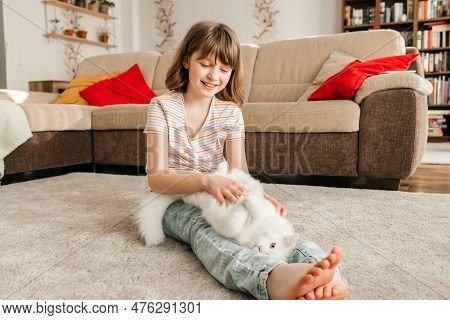 A Cheerful Teenage Girl Plays On The Floor With Her Kitten. The Kitten Lies On The Legs Of The Child