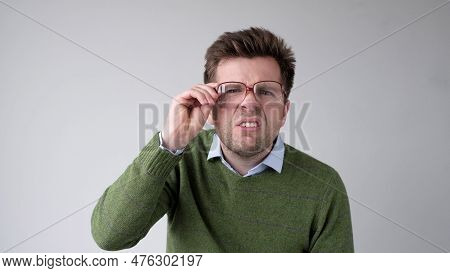 European Young Man With Poor Vision Peers Through His Glasses, Trying To Discern The Information Tha