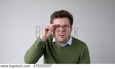 European Young Man With Poor Vision Peers Through His Glasses, Trying To Discern The Information Tha