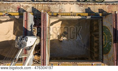 Unloading Dry Cargo Ship By Cranes In Port. Aerial View Of Buldozer Working In Cargo Hold
