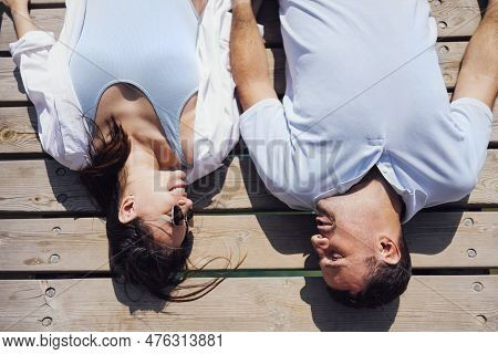 Young Couple In Love In Light Casual Clothes Is Lying On Wooden Bridge. Happy Woman And Man Hug And 