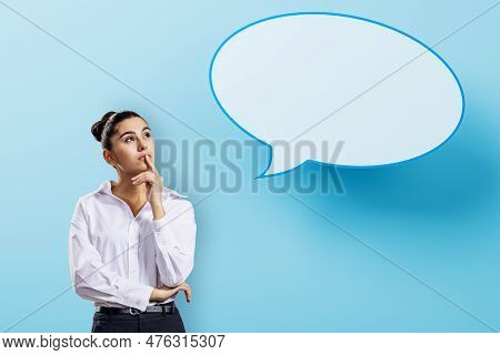 Attractive Pensive European Businesswoman With Speech Bubble On Blue Background. Opinion, Speech And