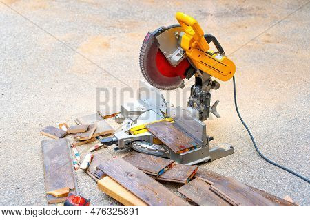 Pile Of Laminate Flooring Offcuts And A Circular Saw Sitting Idle In An Outdoor Setting With Wood Ch