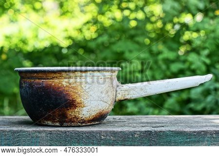 One Old White Enamelled Dirty Metal Saucepan Burnt And Covered In Black Soot Stands On A Gray Table 
