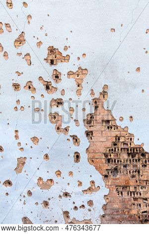 The Wall Of A Building Battered By Rocket Fragments In A War Zone. Shelled Wall. Facade Of A Bombed-