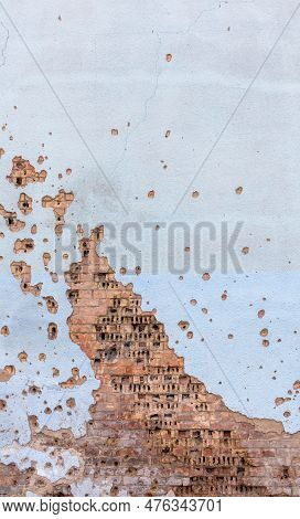 The Wall Of A Building Battered By Rocket Fragments In A War Zone. Shelled Wall. Facade Of A Bombed-