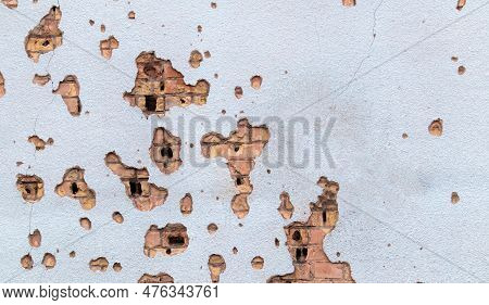 The Wall Of A Building Battered By Rocket Fragments In A War Zone. Shelled Wall. Facade Of A Bombed-