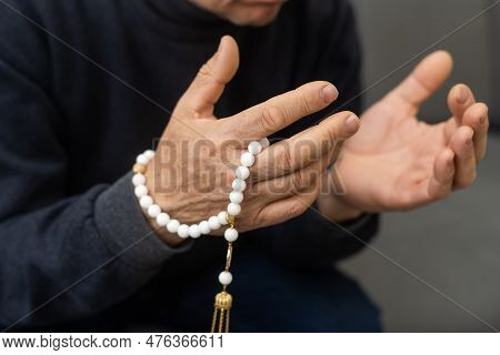 An Elderly Man Prays With A Rosary And The Flag Of The United Arab Emirates