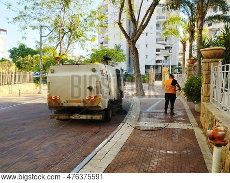 2023 Israel, A Road Sweeper And A Worker Washes Paving Slabs With A Hose While Moving Along The Road
