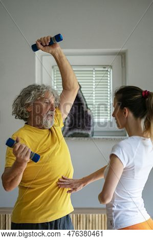 Senior Man In Yellow Shirt Working Out Lifting Dumbbells With A Female Physiotherapist. Activer Reti