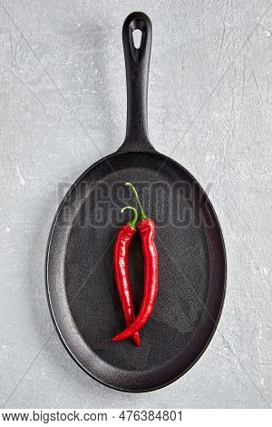 Two Pods Of Red Hot Pepper In The Shape Of A Female Vulva In A Black Cast-iron Frying Pan On A Light