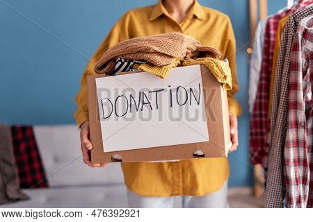 Donation Concept. Woman Holding Donation Box With Donation Clothes In Her Home. Charity. Helping Poo