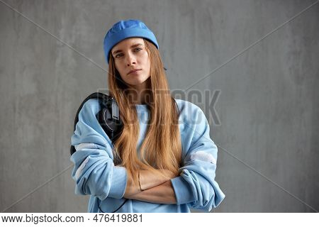 Half-length Portrait Of A Young Pretty Long-haired Girl In A Blue Sweater And Cap With Folded Hands 