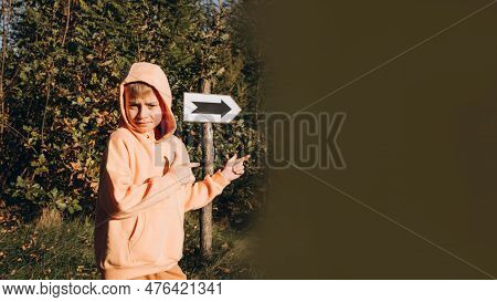 A School-age Boy In The Park Shows The Direction Where To Go And Where The Sign With The Arrow Shows
